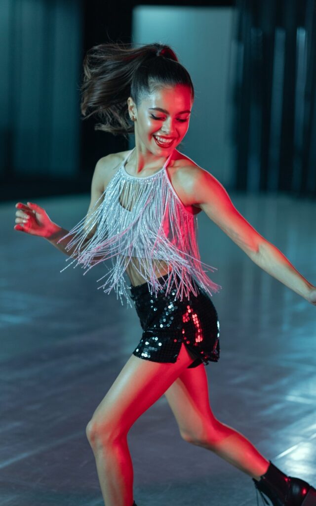 Night street shot with neon signs glowing in the background. Model wears neon pink matching crop top and shorts set layered under a shaggy white faux fur jacket, paired with metallic sneakers. She leans casually on a railing, hair in tousled curls, subtle glossy lips. A mix of luxe and edgy rave style.