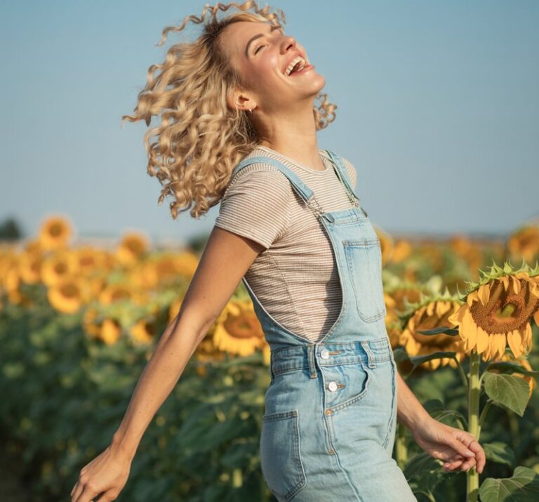 Playful blonde with curly hair, in denim overalls, striped fitted tee, and Converse sneakers. Shot in a sunflower field, natural daylight. She’s laughing mid-step, carefree vibe.