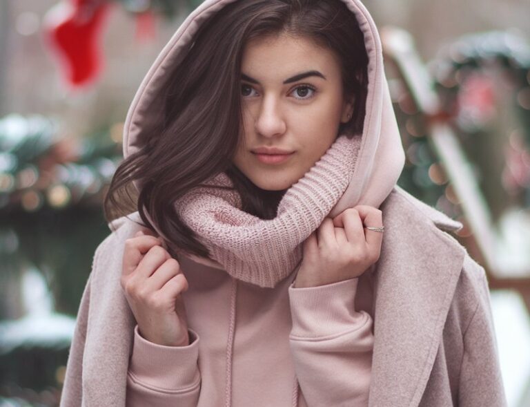 A natural-looking young woman wearing a blush hoodie layered under a classic wool coat. Theme pink christmas outfit