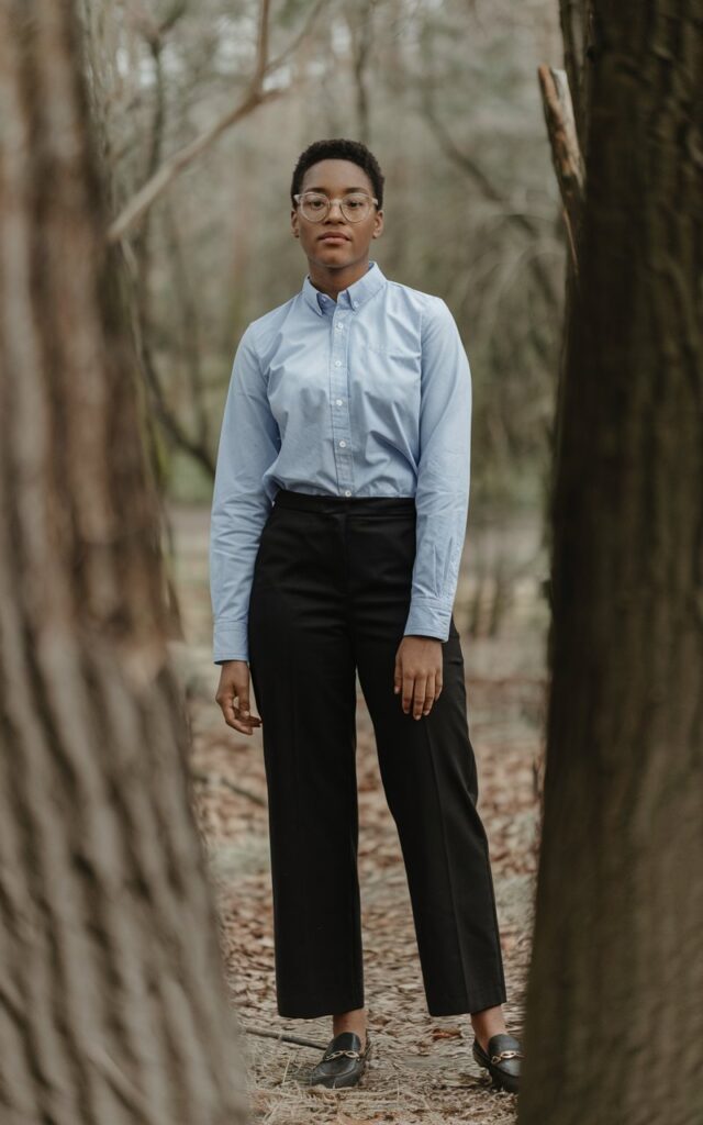 A natural-looking young woman wearing a crisp oxford shirt paired with black straight-leg pants and loafers. Theme tomboy outfits