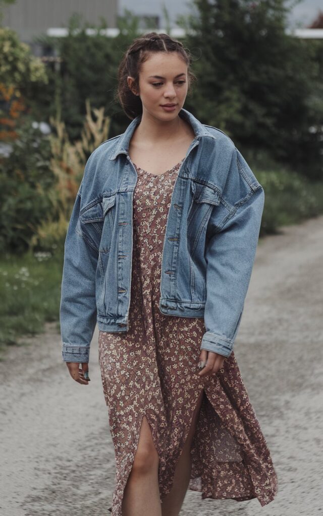 A natural-looking young woman wearing a denim jacket layered over a midi dress. Theme fashion inspo outfits