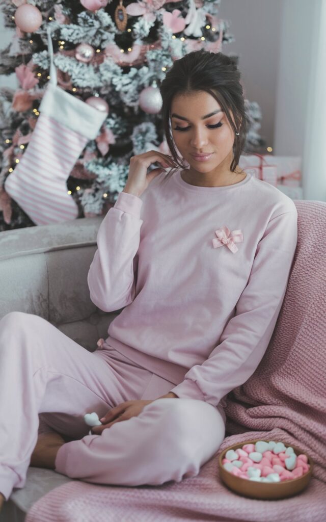A natural-looking young woman wearing a monochrome pink lounge set styled for a cozy Christmas morning. Theme pink christmas outfit