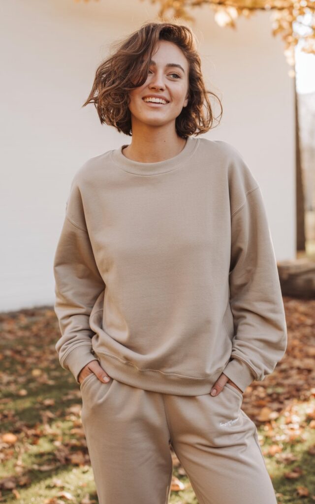 A natural-looking young woman wearing a neutral crewneck sweatshirt with matching sweatpants. Theme casual fall outfits