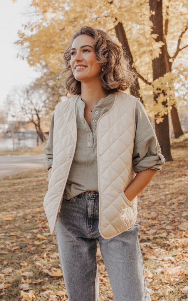 A natural-looking young woman wearing a quilted vest with a Henley top and relaxed jeans. Theme casual fall outfits