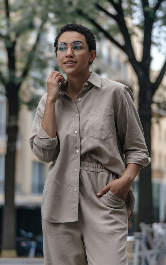 A natural-looking young woman wearing a simple button-down shirt with sleeves rolled up and relaxed-fit pants. Theme tomboy outfits