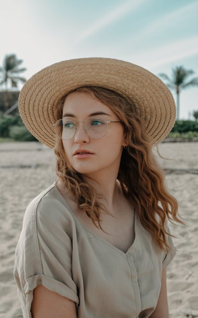 A natural-looking young woman wearing a simple outfit styled with a straw hat. Theme beach outfits