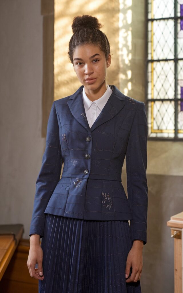 A natural-looking young woman wearing a structured blazer paired with a pleated midi skirt. Theme church winter outfit