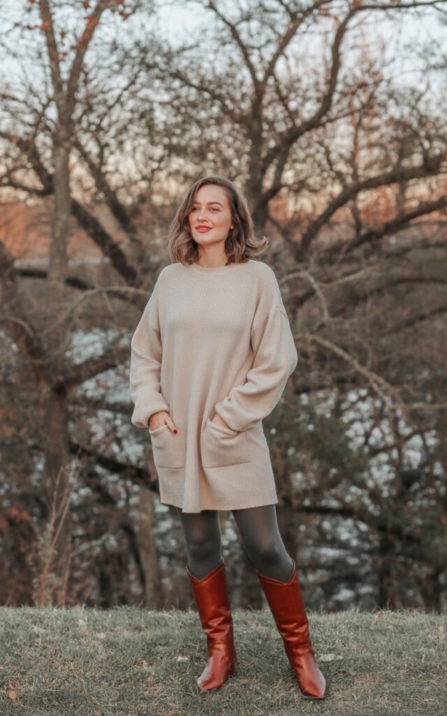 A natural-looking young woman wearing a sweater dress styled with tights and knee-high boots. Theme cold weather outfits