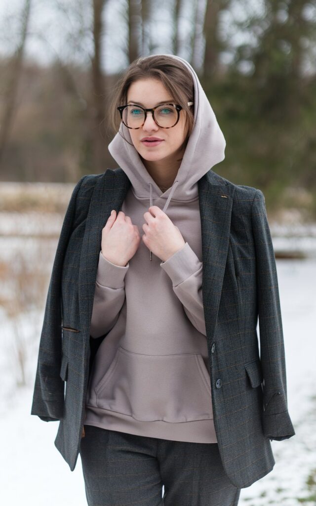 A natural-looking young woman wearing a tailored blazer styled over a cozy hoodie with trousers. Theme winter fashion outfits