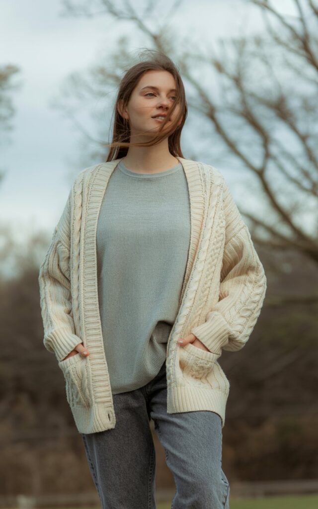 A natural-looking young woman wearing an oversized cardigan over a thermal tee with relaxed-fit jeans. Theme cold weather outfits