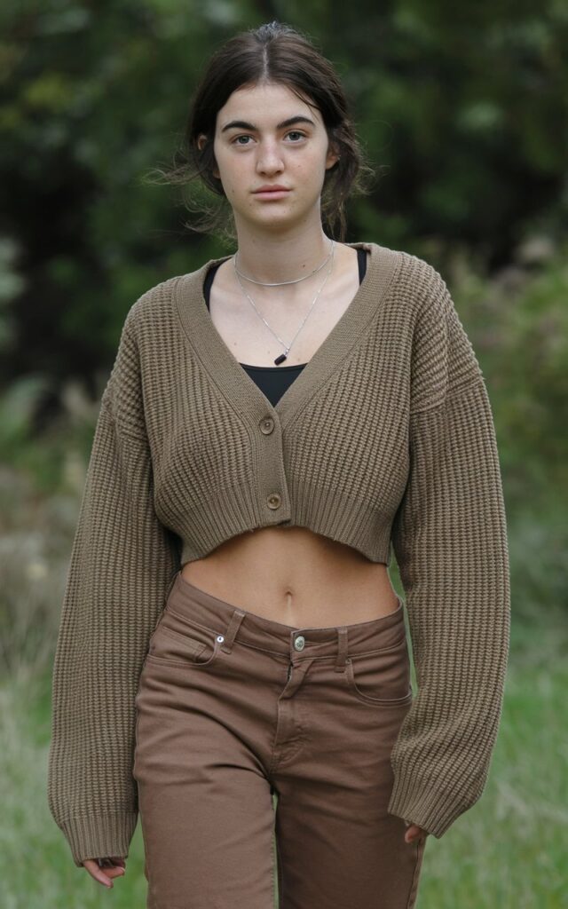 A natural-looking young woman wearing brown pants paired with a cropped cardigan for a modern, feminine outfit. Theme brown pants outfit for women