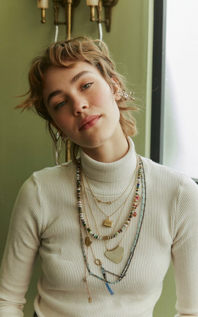 A natural-looking young woman wearing chunky necklaces layered over a turtleneck. Theme quirky fashion
