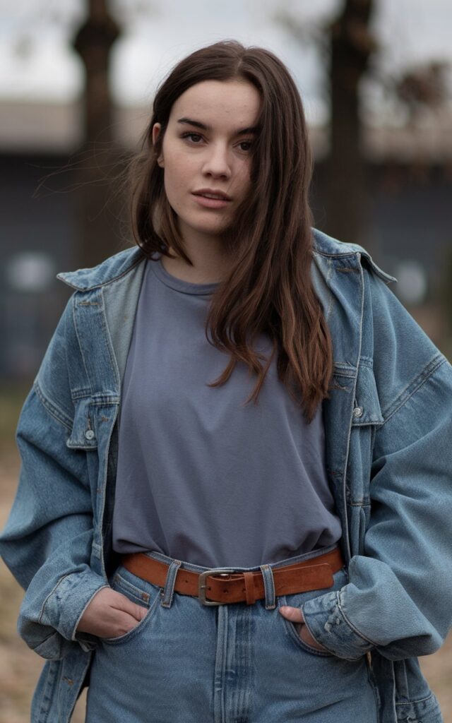 A natural-looking young woman wearing loose-fit jeans with a tucked-in basic tee and a leather belt. Theme tomboy outfits