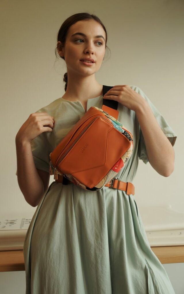 A natural-looking young woman wearing quirky fashion belt bag cinched over a flowy dress. Theme quirky fashion