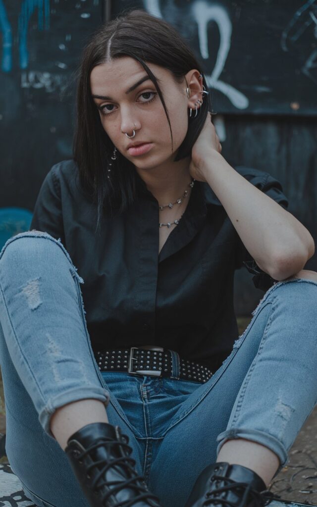 A natural-looking young woman wearing skinny jeans with a studded belt and combat boots. Theme emo outfits