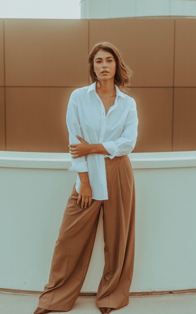 A natural-looking young woman wearing wide-leg brown pants paired with a crisp white button-down shirt, styled in a polished yet relaxed way. Theme brown pants outfit for women