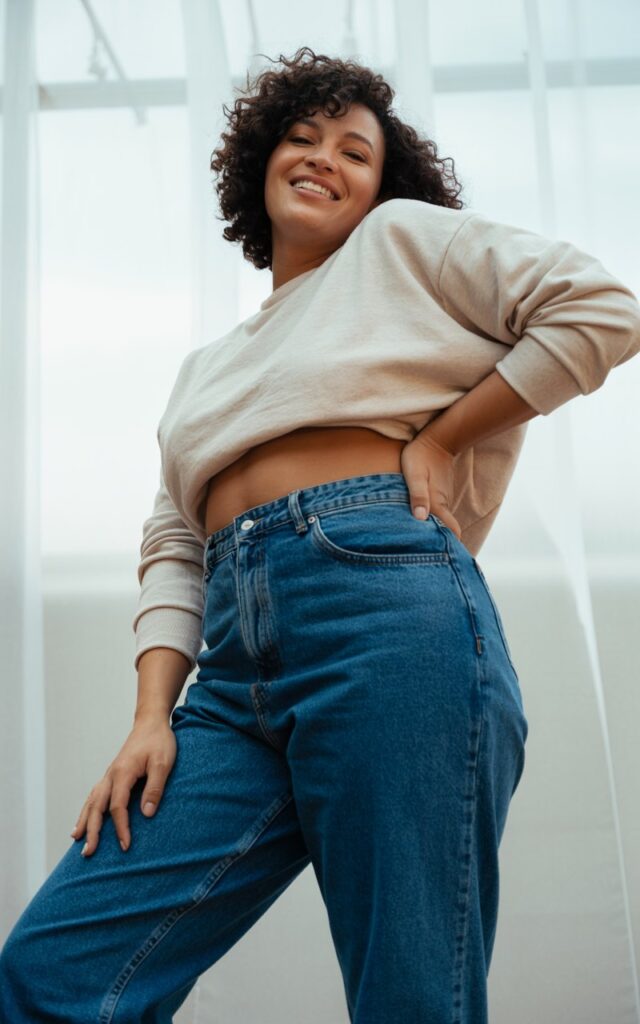 "A natural-looking curvy young woman wearing high-waisted jeans with a cropped sweater. Theme: curvy outfits."