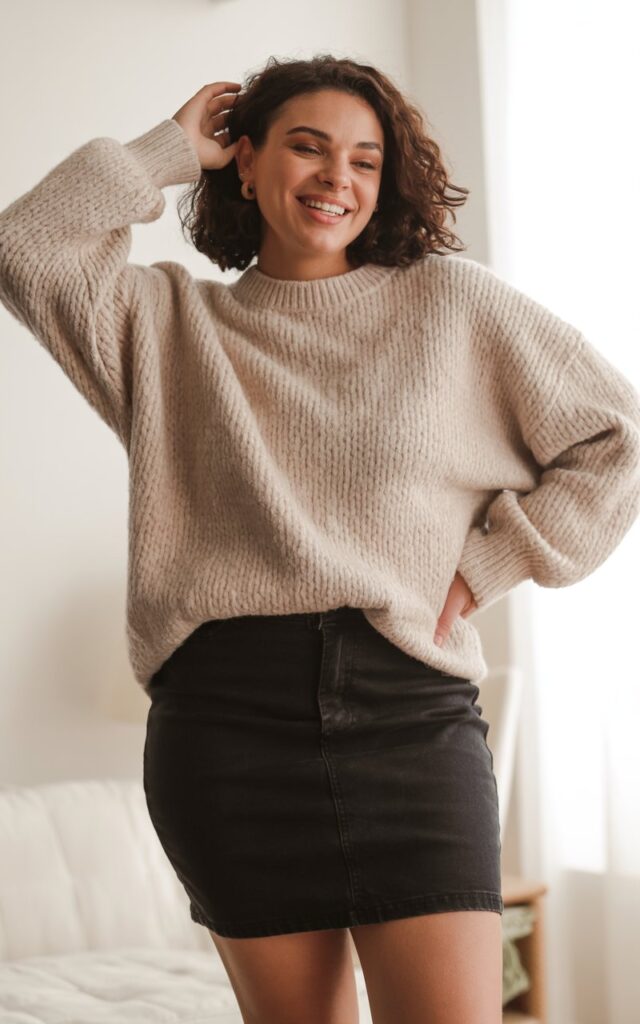 "A natural-looking young curvy woman wearing a chunky knit sweater with a mini skirt. Theme: curvy outfits."